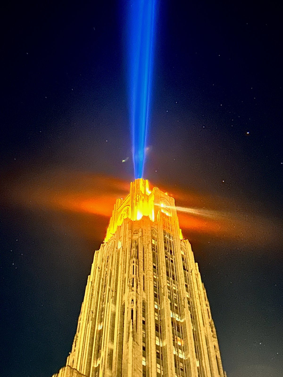 The Cathedral of Learning illuminated at night beneath a blue beam